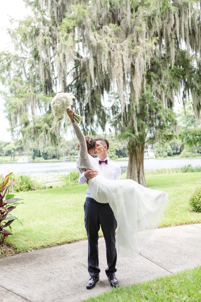 Christmas in July SS 167 - Christmas Themed Wedding Inspiration - Inspiration Shoot groom holding the bride in his arms and kissing while she holds her bouquet in the air