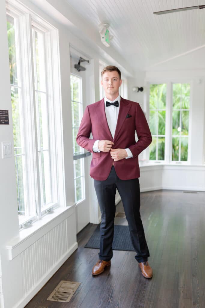 Christmas in July SS 33 - Christmas Themed Wedding Inspiration - Inspiration Shoot Groom in tuxedo facing the camera. He is wearing a red coat with a black hankerchief in the pocket.