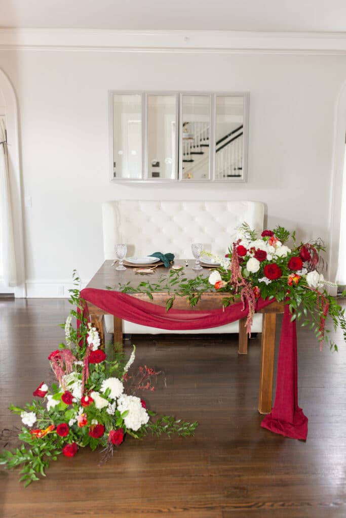 Christmas in July SS 64 - Christmas Themed Wedding Inspiration - Inspiration Shoot the sweetheart table with a white booth and red and green details and flowers on the table to match the christmas themed wedding inspiration shoot.