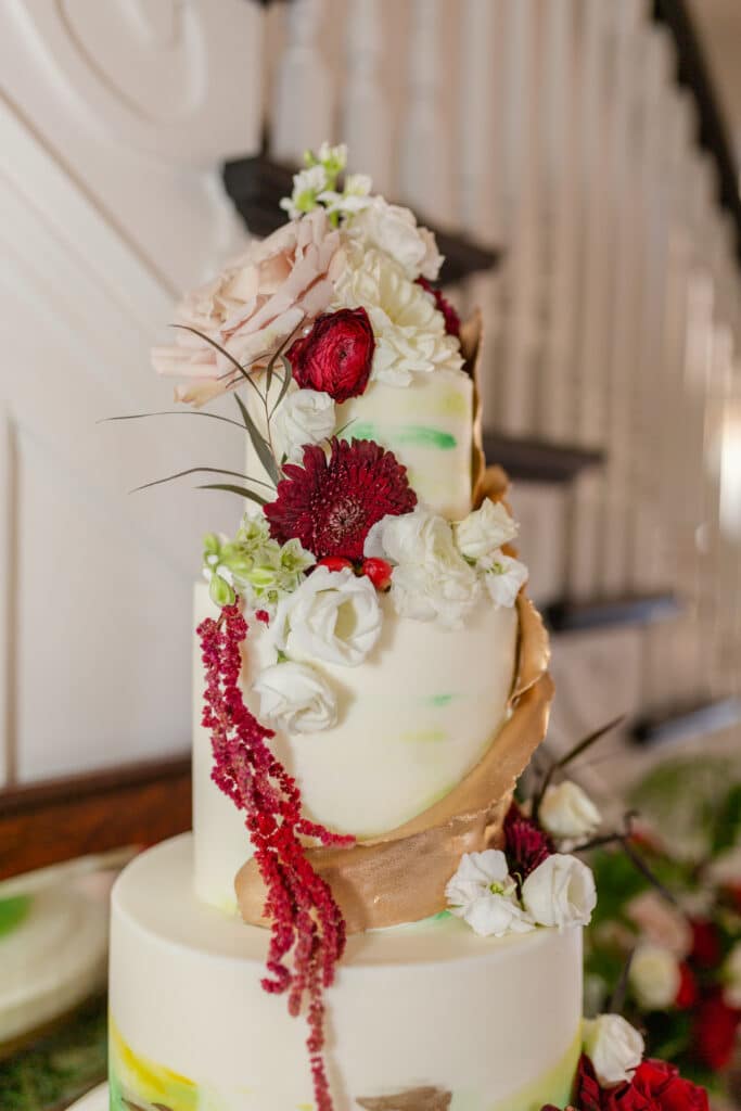 Christmas in July SS 89 - Christmas Themed Wedding Inspiration - Inspiration Shoot Christmas in July wedding cake. There are red and white flowers draping down the white frosted cake. It's 3 tiers and there are flowers on the top tier.