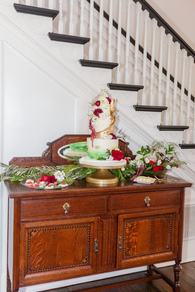 Christmas in July SS 93 - Christmas Themed Wedding Inspiration - Inspiration Shoot the cake table decorated with florals and greenery with the cake on a gold cake stand for the christmas themed wedding inspiration shoot.