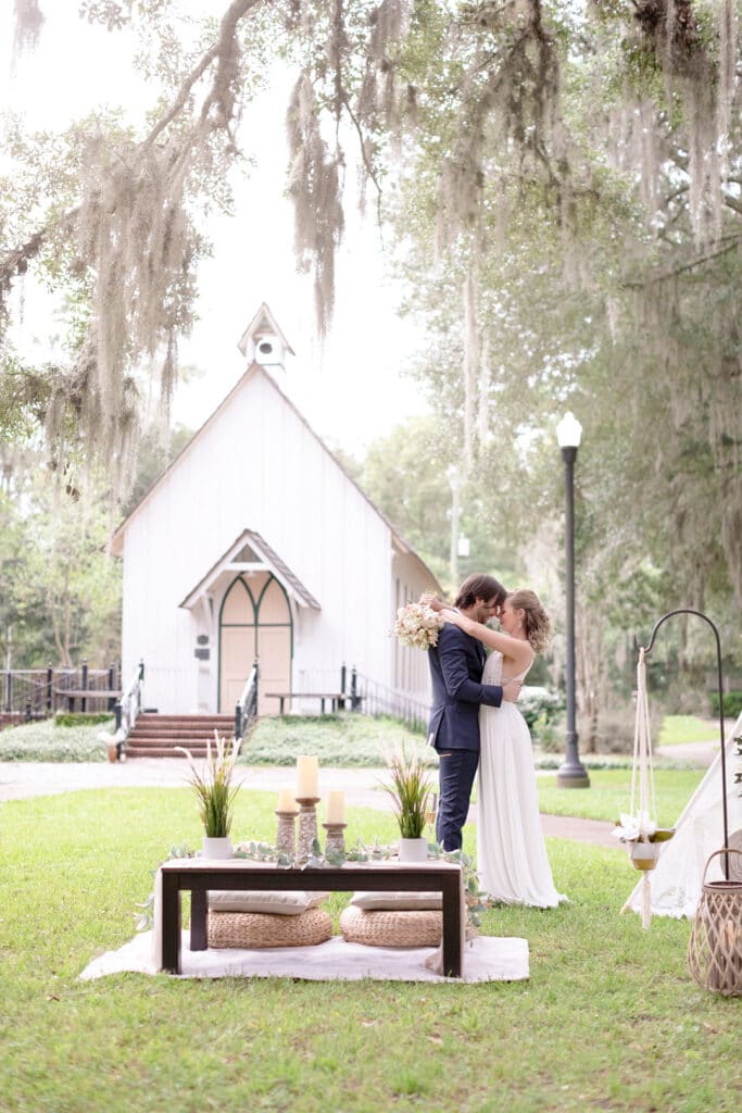 bride and groom forehead to forehead standing together next to their picnic set up with the venue in the background