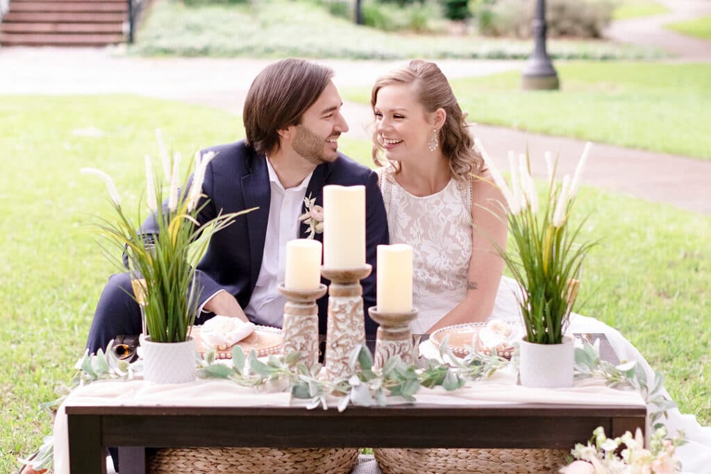 bride and groom looking at each other while sitting at their picnic set up for the picnic wedding inspiration shoot
