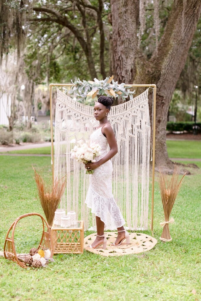 bride standing in front of a macrame backdrop with wicker furniture surrounding for the picnic wedding inspiration shoot.