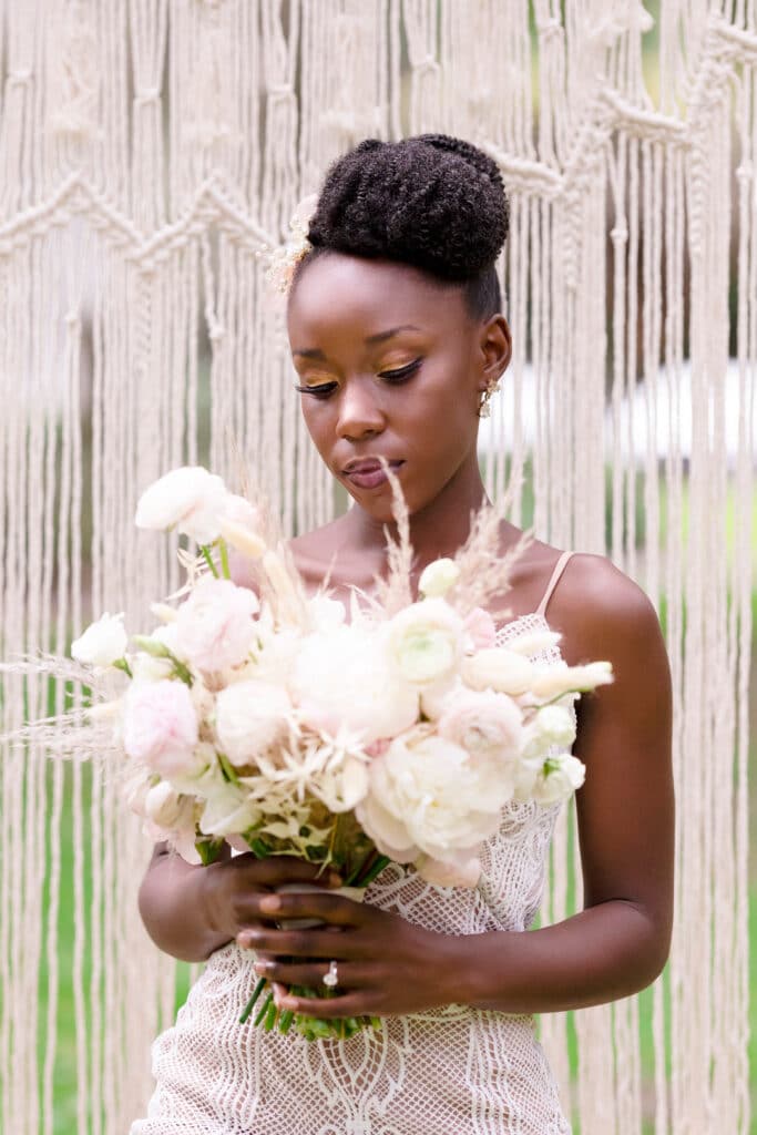 bride holding her white and pink bouquet of flowers with macrame backdrop behind her