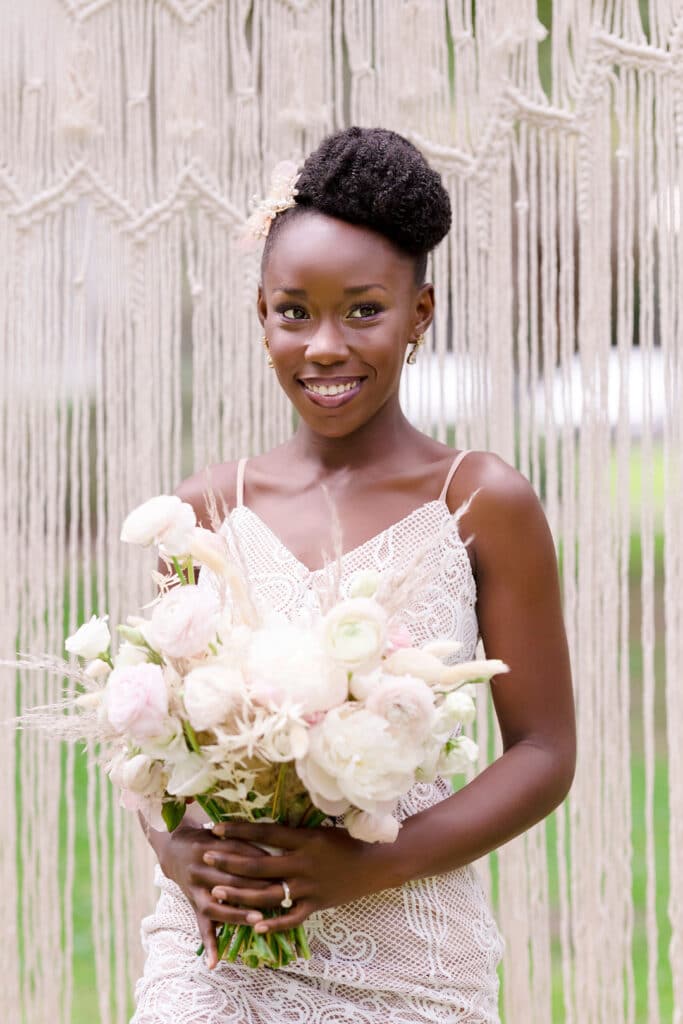 bride smiling and holding her pink and white bouquet of flowers with a white macrame backdrop behind her