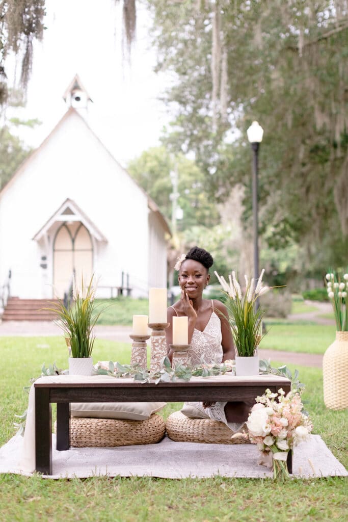bride sitting at picnic set up with decor on the table and the venue in the background