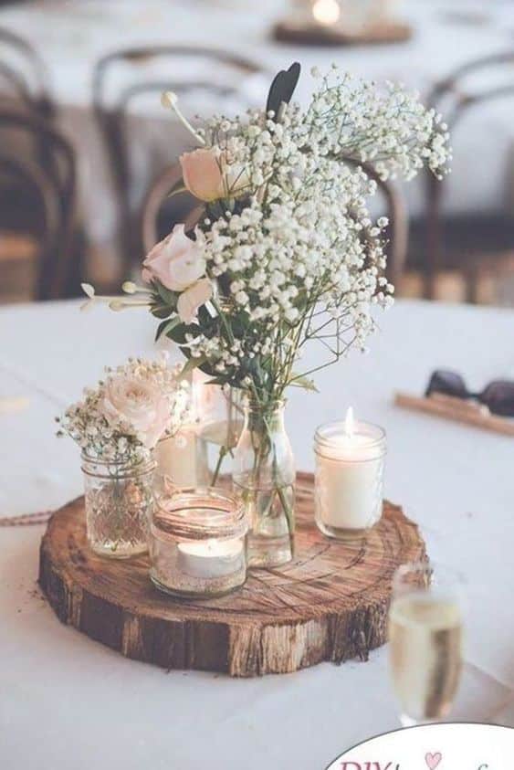 table centerpiece with wood slive and candles in miscellaneous glass containers with candles and small sprigs of flowers including babys breath