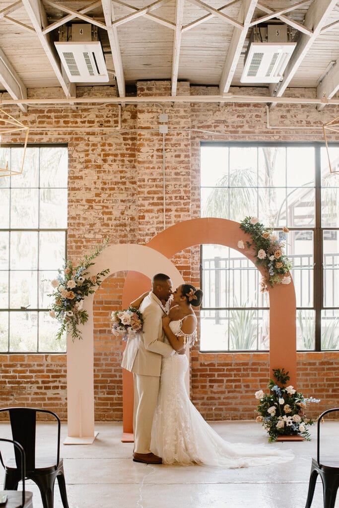 Summer Urban Loft Wedding Inspiration Grace Jicha Venue At The Block Wedding BrideandGroom 13 websize low - Urban Loft Wedding Inspiration - Styled Shoot bride and groom holding each other at the end of the aisle in front of the two large pink arches for the urban loft wedding inspiration styled shoot.