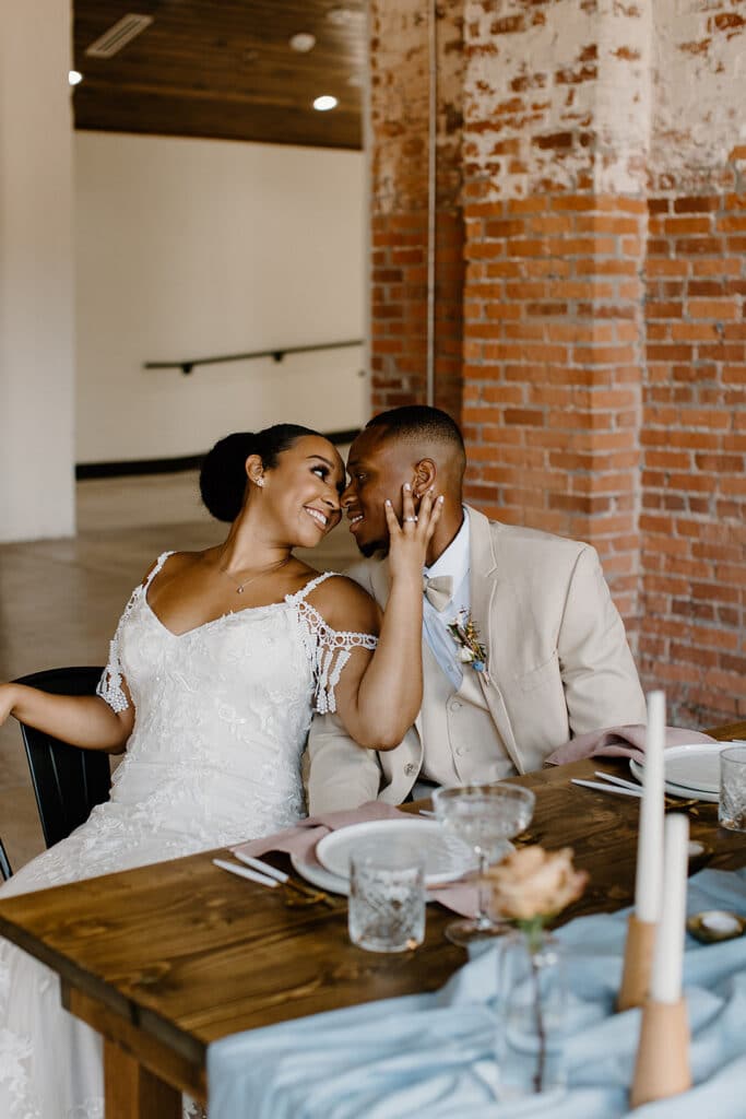 Summer Urban Loft Wedding Inspiration Grace Jicha Venue At The Block Wedding BrideandGroom 33 websize low 1 - Urban Loft Wedding Inspiration - Styled Shoot bride holding the grooms face as they are sitting at the reception table.