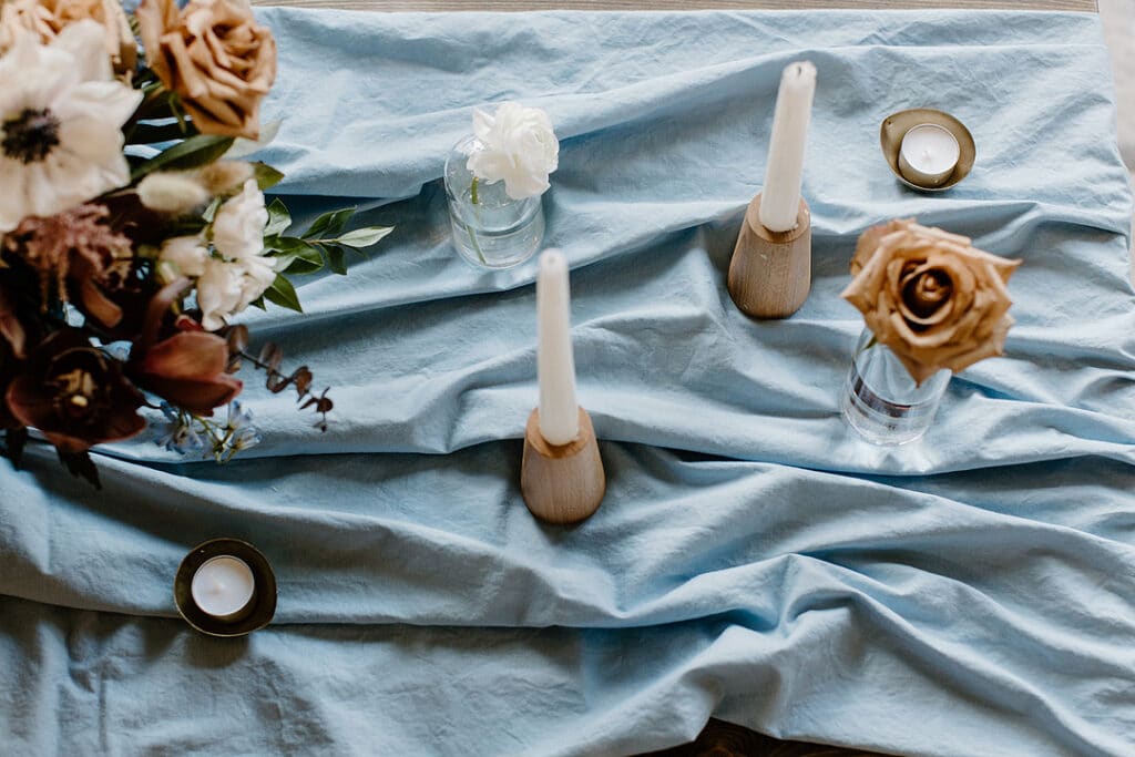 Summer Urban Loft Wedding Inspiration Grace Jicha Venue At The Block Wedding Tablescape 19 websize low - Urban Loft Wedding Inspiration - Styled Shoot blue tablecloth with candles and vases with singular flowers and a large flower centerpiece.