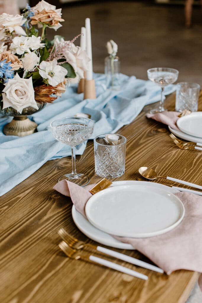 Summer Urban Loft Wedding Inspiration Grace Jicha Venue At The Block Wedding Tablescape 5 websize low 1 - Urban Loft Wedding Inspiration - Styled Shoot the plates and silverware with the blue tablecloth runner and flower centerpiece on the reception table.