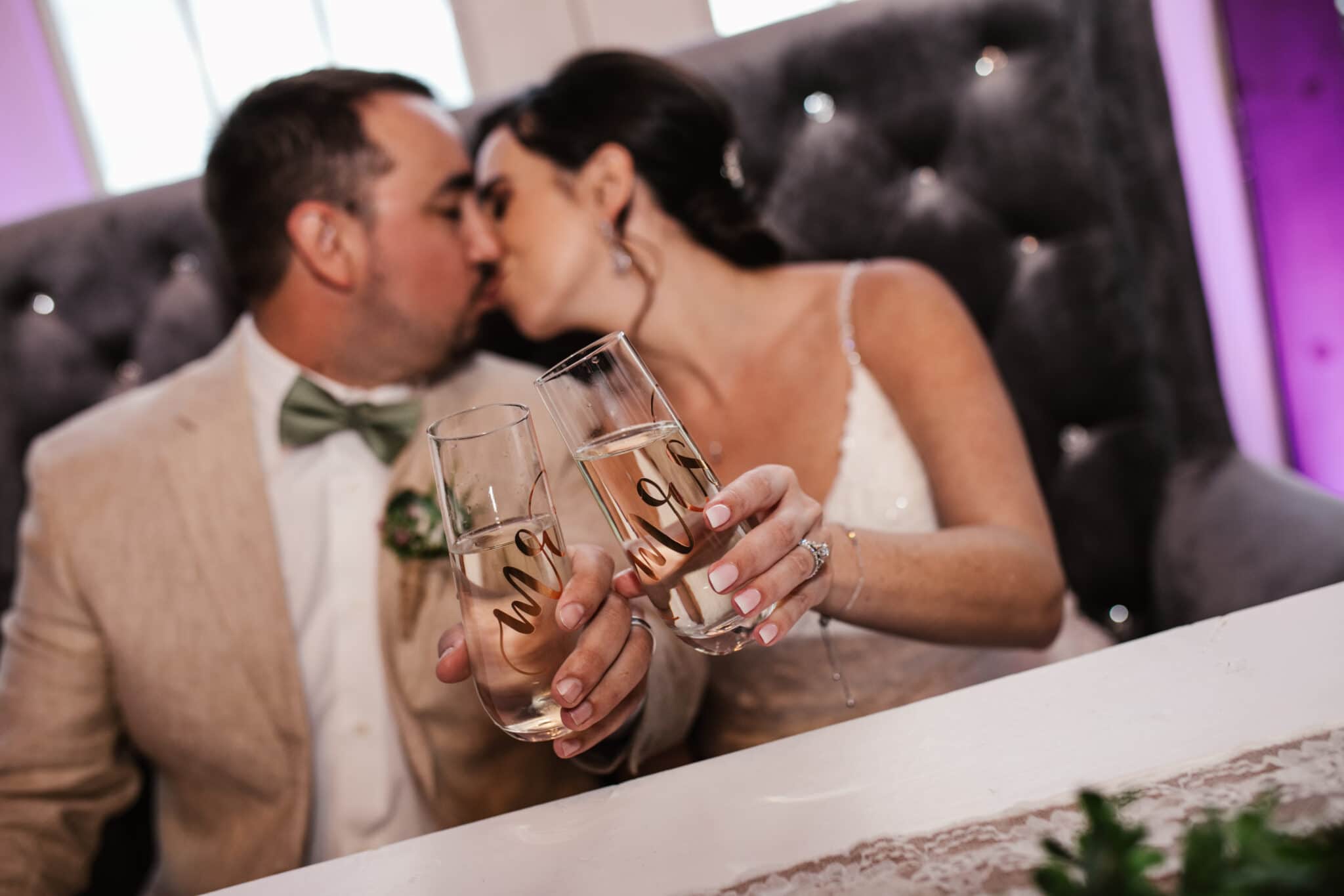 the bride and groom kissing and holding their mr. and mrs. glasses together.