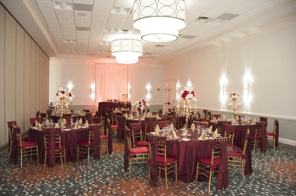 wedding reception set up in ballroom with large modern chandeliers and red linens on round tables