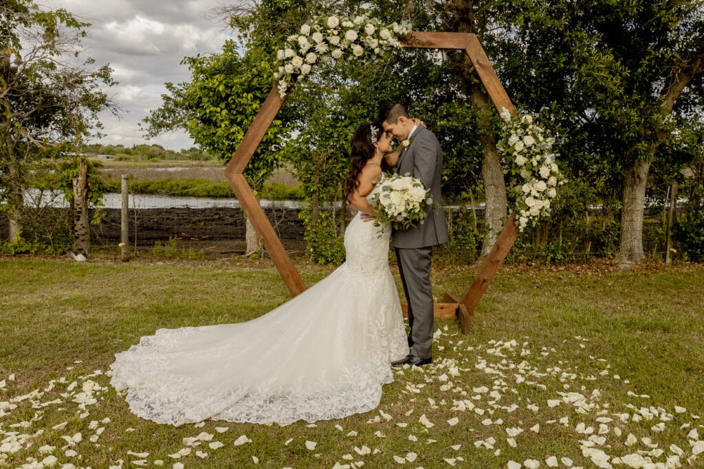 Bride and groom in front of a wooden arch. They have their faces together in embrace