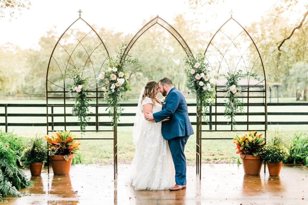 A bride and groom almost kissing under an arch adorned with flowers