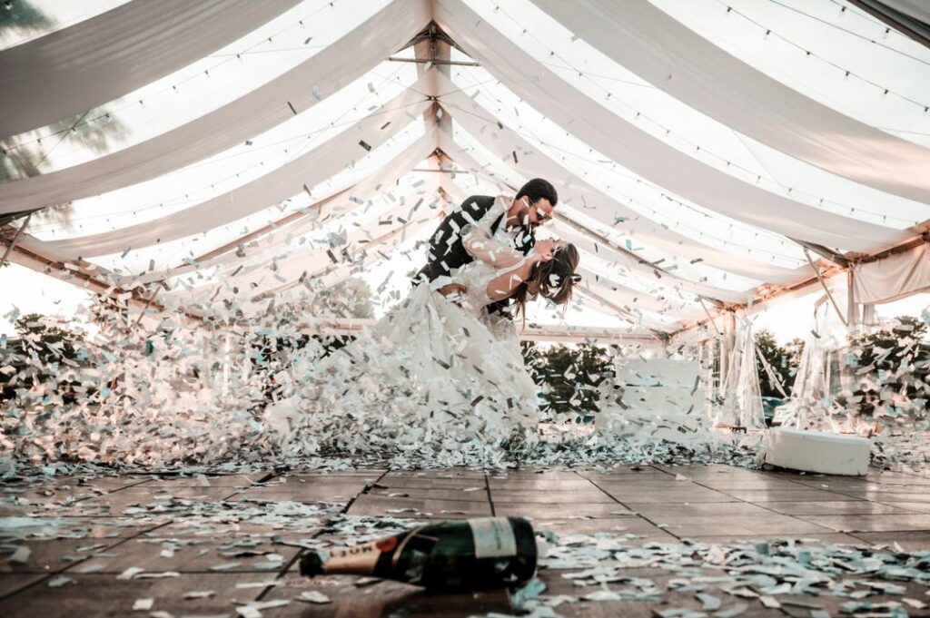 bride and groom dancing under white tent with confetti flying around them