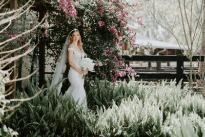 Bride standing among ferns in front of a tree with pink flowers