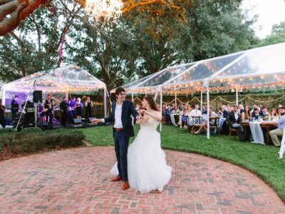 Bride and groom during their first dance. There is a band under a tent as their guests watch.
