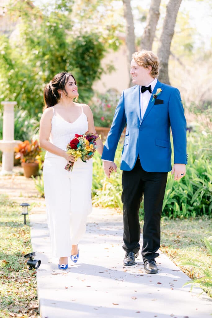Bride and groom walking together smiling. His blazer is royal blue and her shoes match.