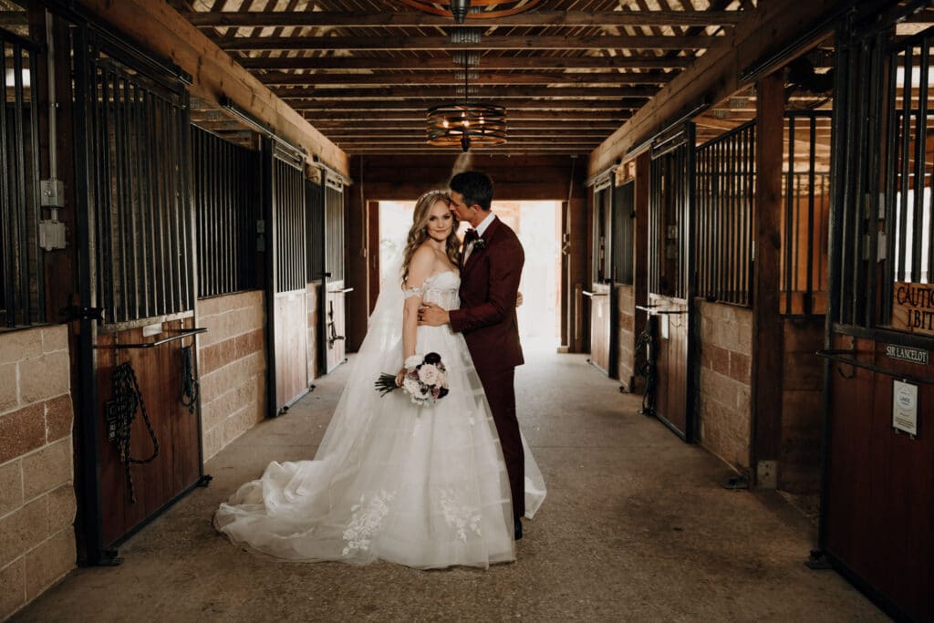 Bride and groom embracing inside a horse stable