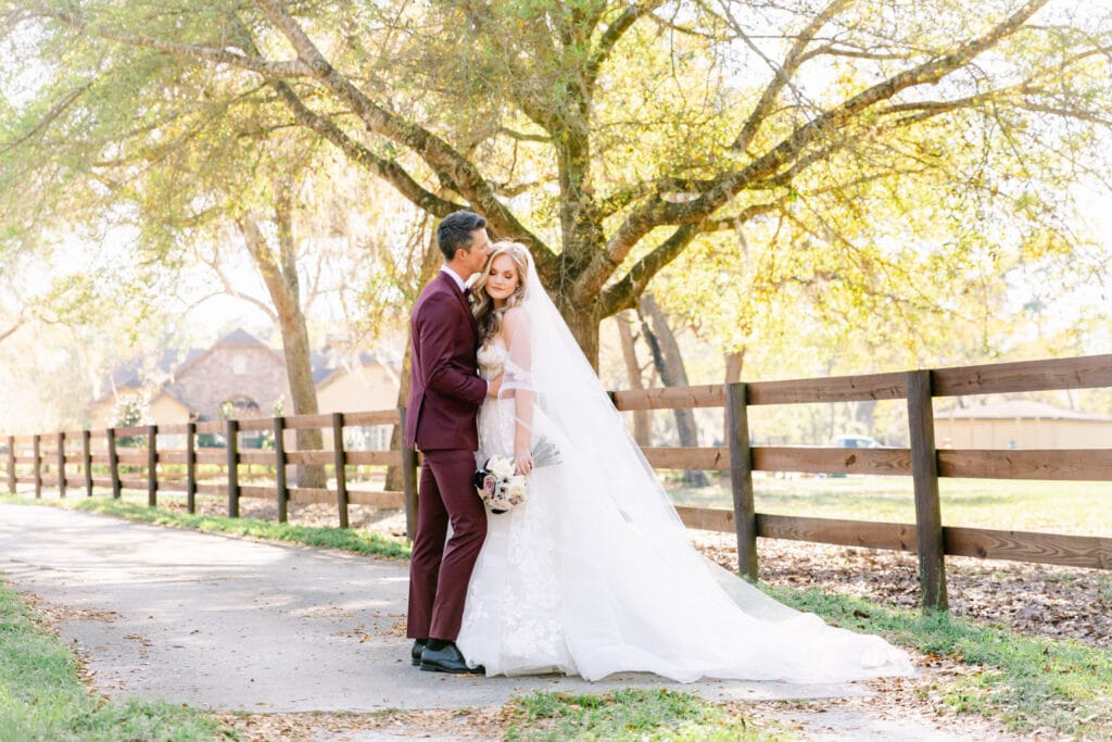 Groom kissing his bride's head outside at a stable