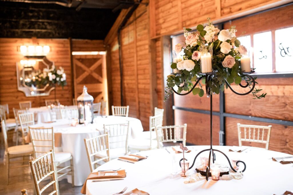 Inside reception in a barn. We see tables with floral arrangements and lanterns