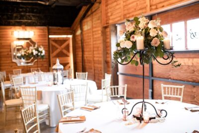 Inside reception in a barn. We see tables with floral arrangements and lanterns