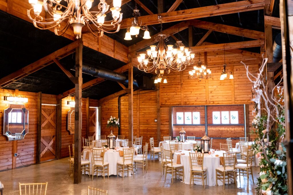 Inside reception in a barn. We see tables with floral arrangements and lanterns
