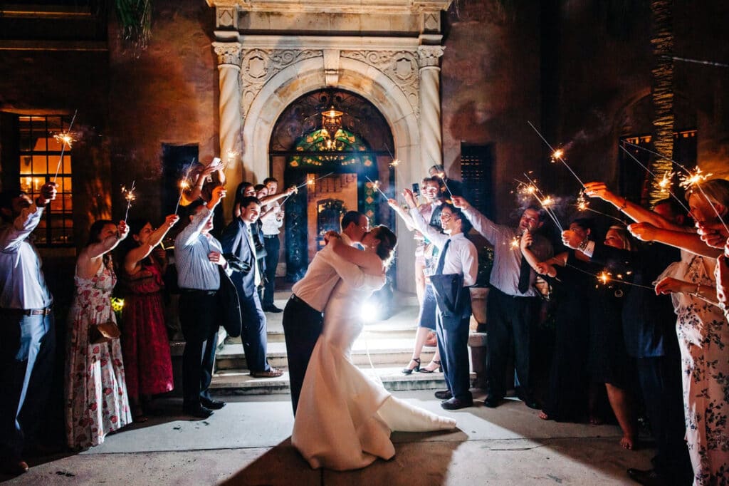 A bride and groom kissing. Their guests are surrounding them with sparklers