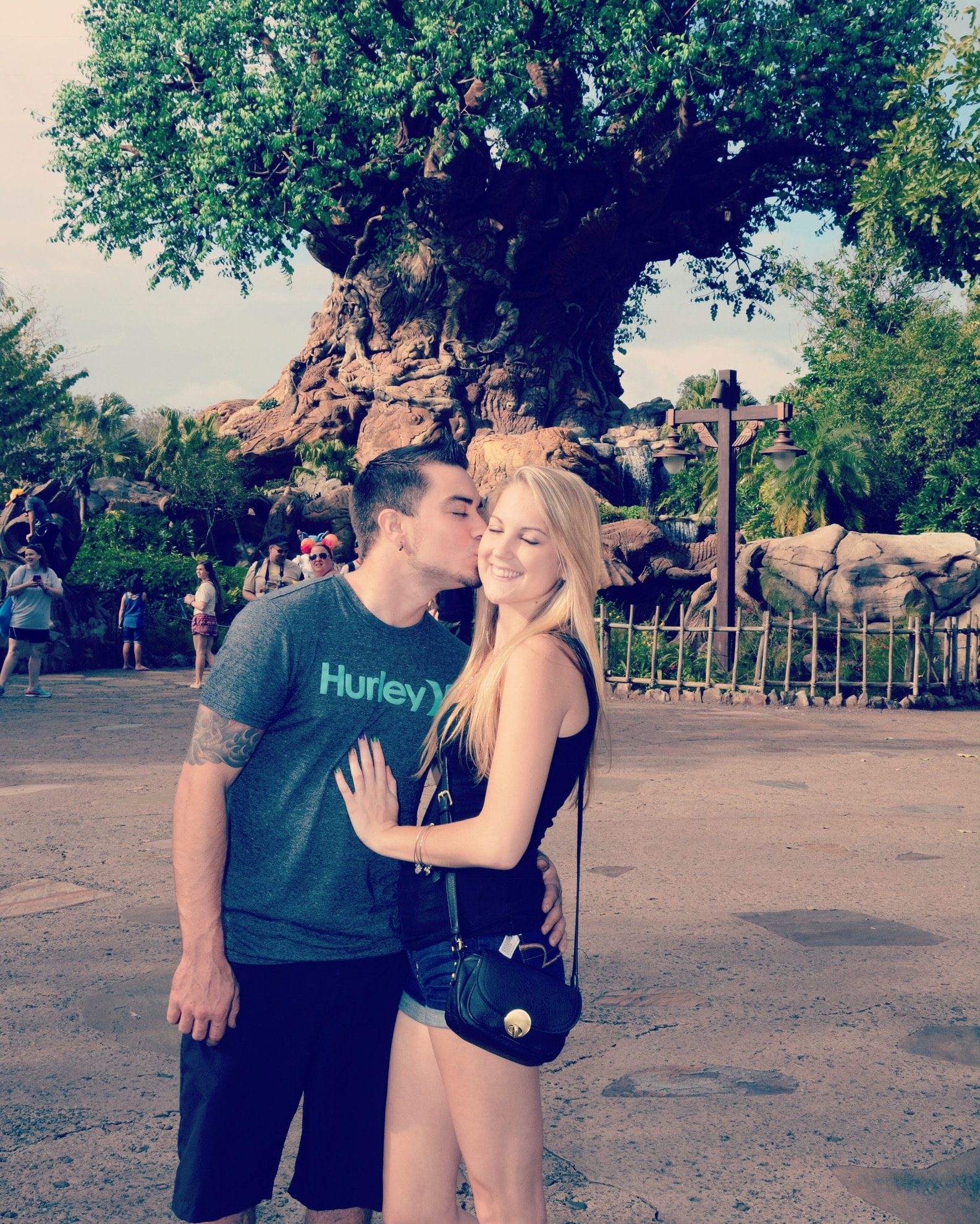 bride-to-be smiling while groom-to-be kisses her on the cheek at disney's animal kingdom in front of the tree of life.