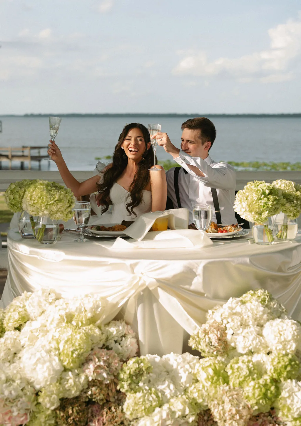 Couple enjoying dinner by the waterfront surrounded by beautiful floral arrangements.