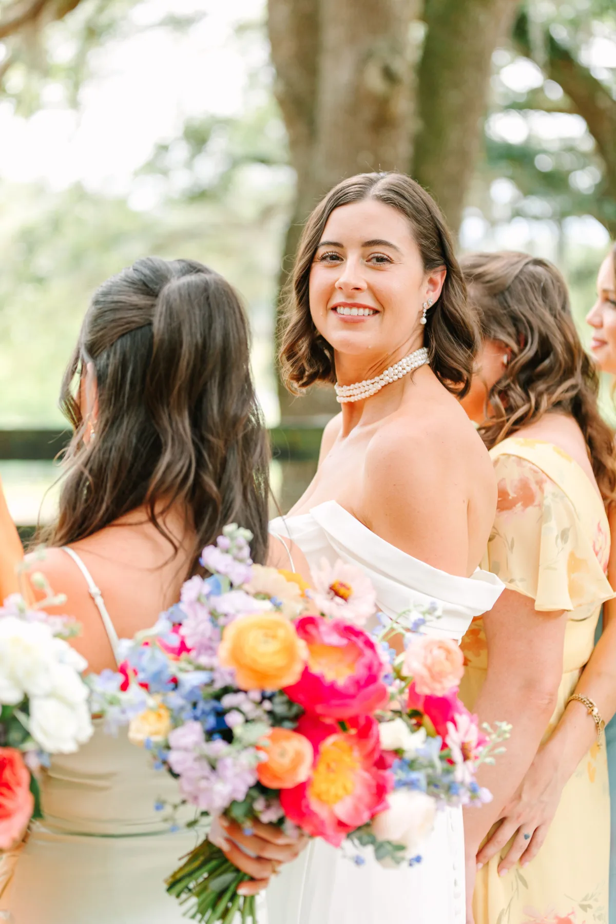 Elegant bride holding a colorful wedding bouquet with pastel and vibrant flowers at an outdoor wedding.