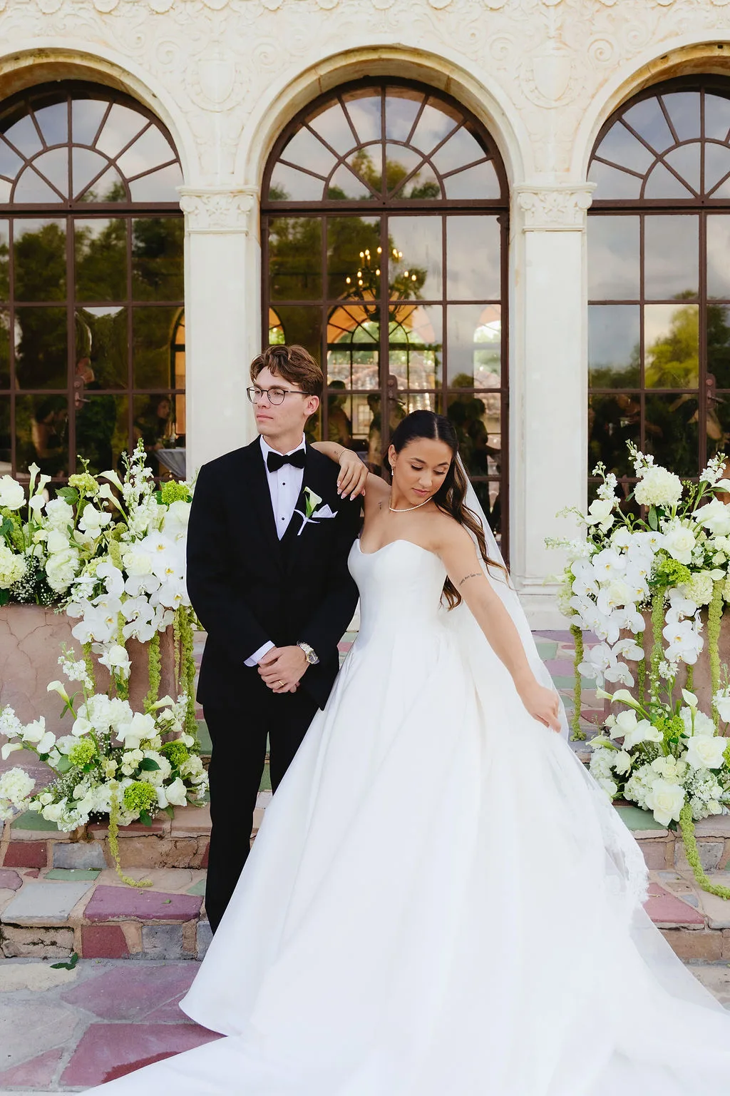 Bride and groom surrounded by lush white and green wedding flowers at an elegant luxury venue.