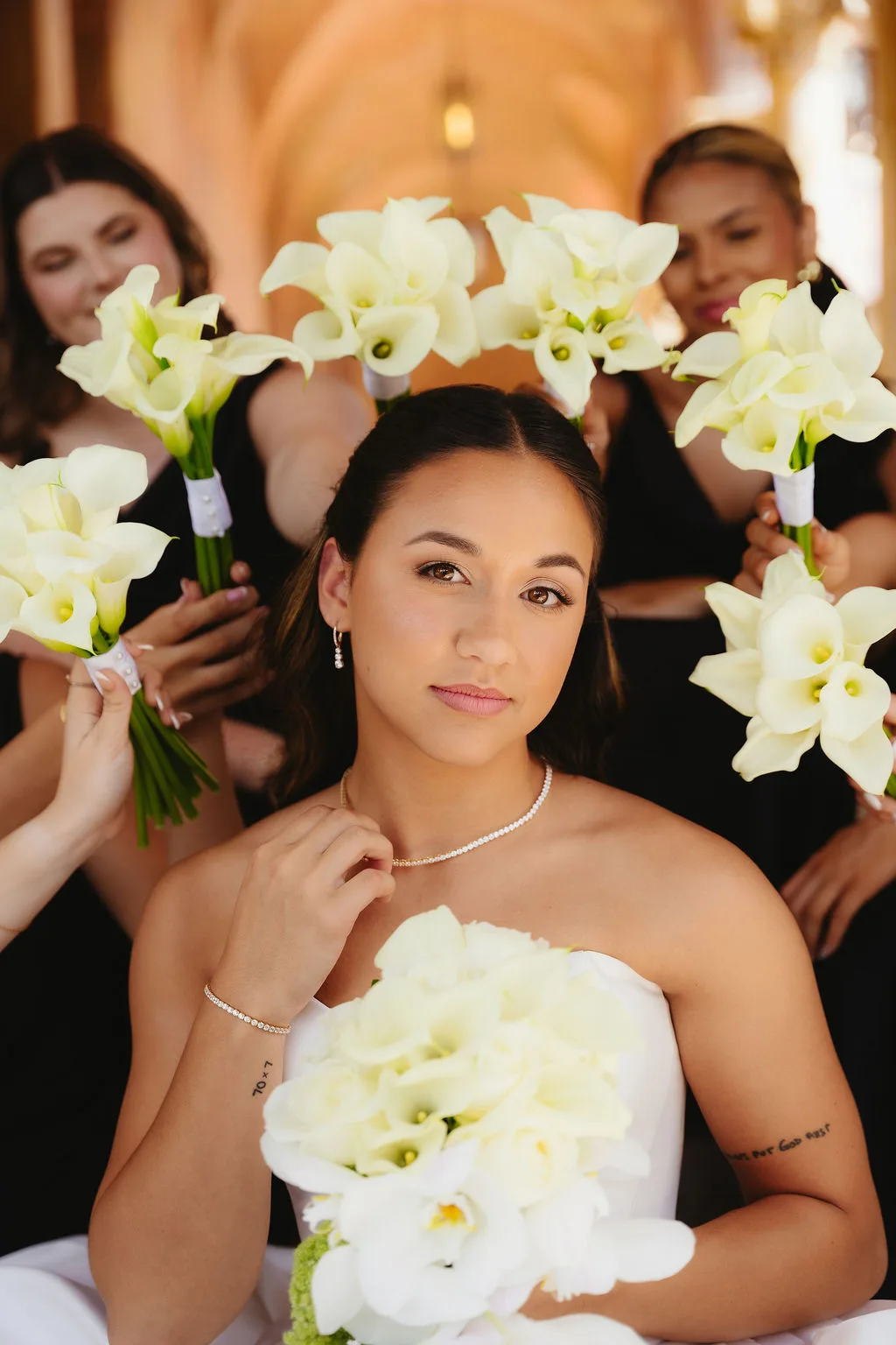 Bride holding a white floral bouquet surrounded by bridesmaids with matching white calla lily bouquets.
