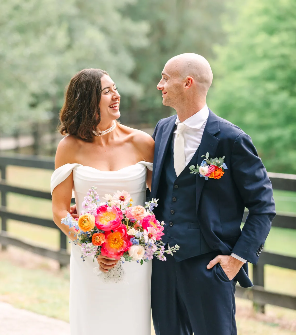 Bride and groom with a vibrant colorful wedding bouquet and matching floral boutonnière at an elegant outdoor wedding.