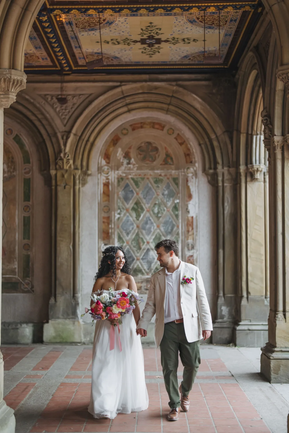 Bride and groom walking through an elegant historic venue with a colorful romantic wedding bouquet.