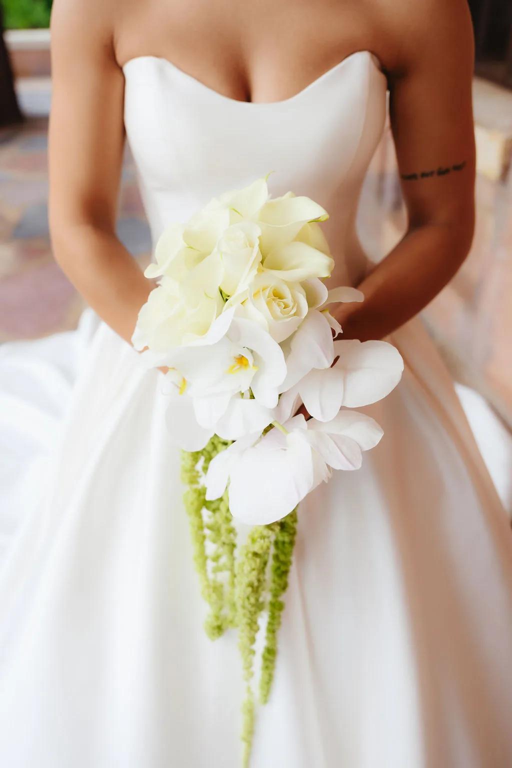 Bride holding an elegant cascading white bridal bouquet of roses and orchids with trailing green flowers.