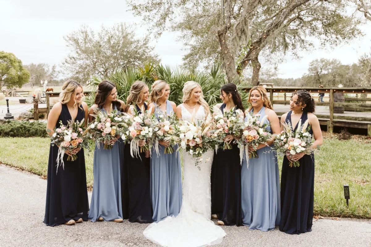 Bride and bridesmaids holding lush blush, ivory, and greenery wedding bouquets at an outdoor Florida wedding.