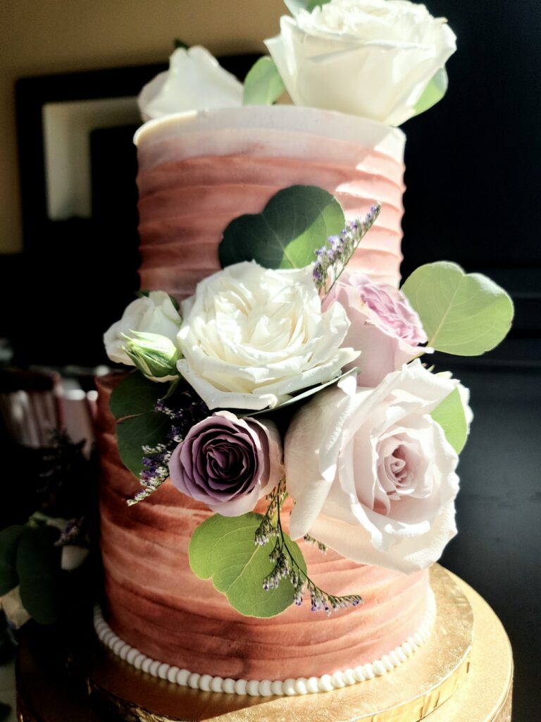 Pink cake with white and lavender roses and greenery by Butter Bliss Bakeshop