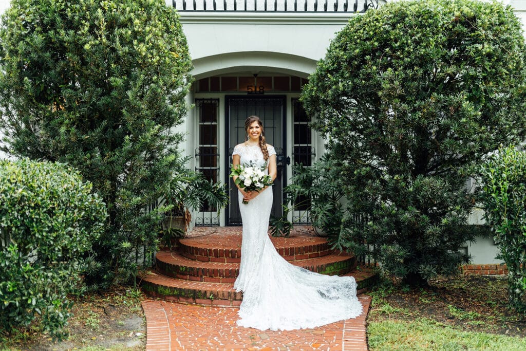 bride in lace dress holding bouquet and standing on brick stairs in front of historic wedding venue in deland florida