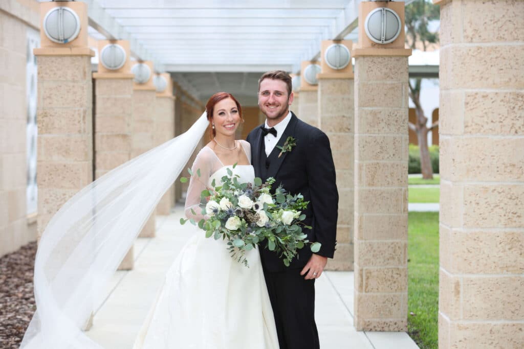 Red headed bride with a flowing veil. She is standing beside her smiling groom and she's holding her ivory and green bouquet