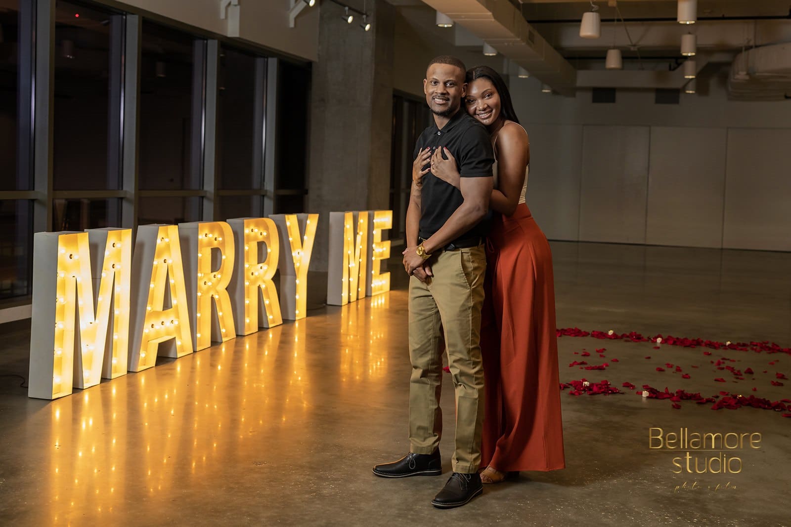 bride-to-be hugging the groom-to-be from behind in front of their marry me sign from the proposal.