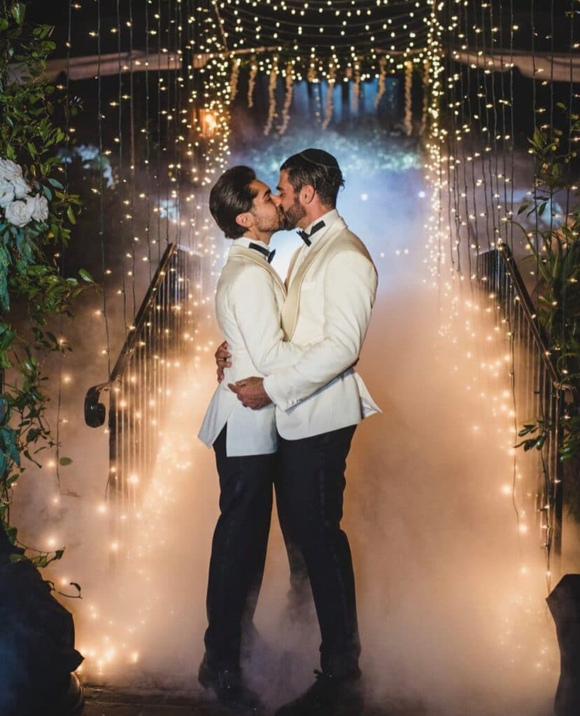 Men kissing after their wedding. They are both wearing white coats and black pants