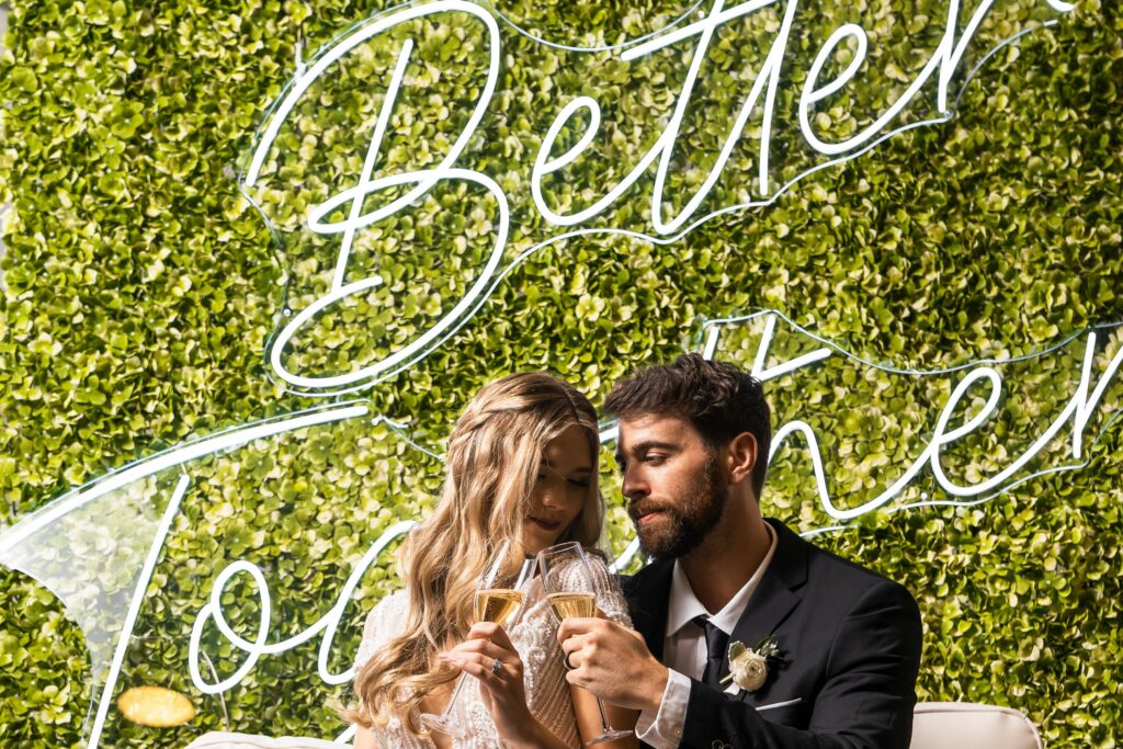 bride and groom embracing in front of hedge wall with sign that says better together