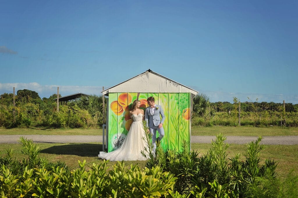 bride and groom standing in front of small building with peach mural painted on it
