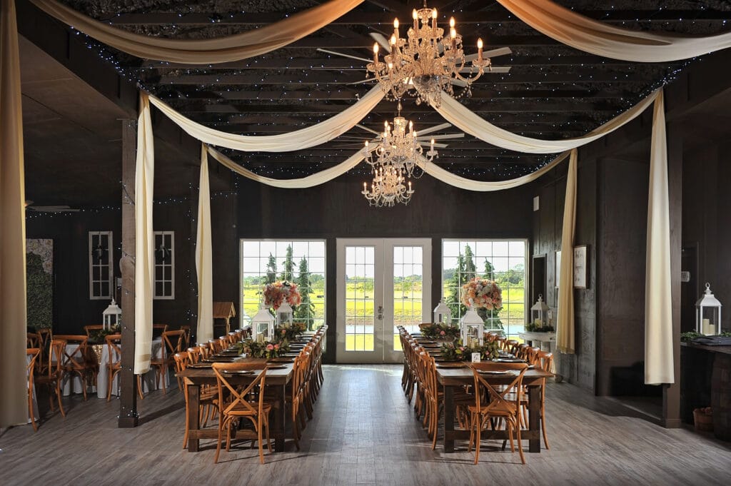 wedding reception in barn with large chandeliers and long wood tables