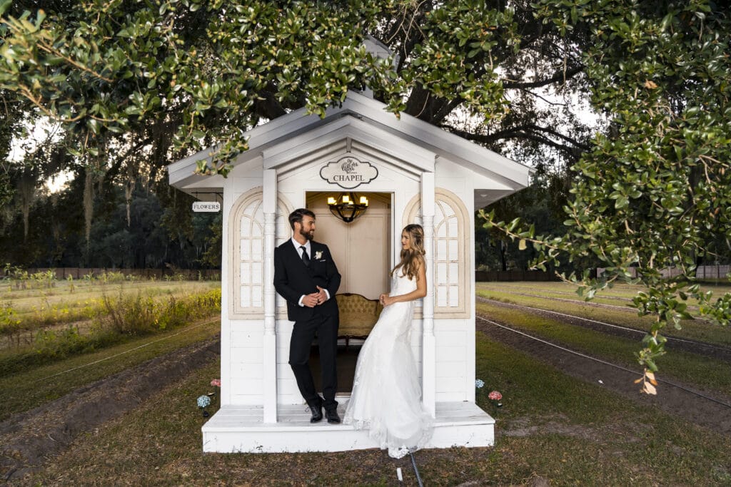 bride and groom standing in front of small white building
