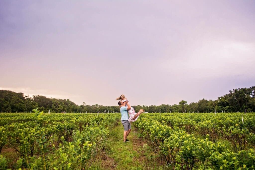 man holding woman in middle of blueberry field