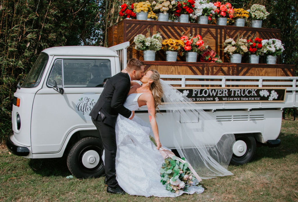 bride and groom kissing in front of white delivery truck carrying colorful flowers